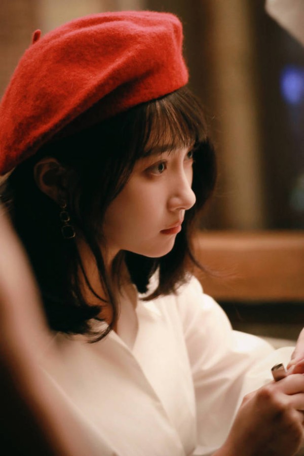 关晓彤头戴红色贝雷帽，身着白衬衫，侧眸凝视，在暖光中尽显温柔文艺的气质。