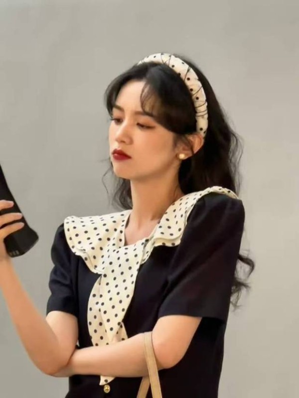 搜狐娱乐讯 近日，周也一组复古风随拍曝光。她穿波点翻领裙，戴发箍，手持大哥大，尽显90年代甜妹感。